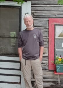 Photo of Author Jeffrey M. Holden in front of log cabin 